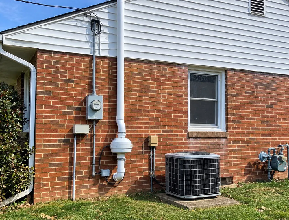 Exterior radon mitigation fan and vent pipe on a brick-and-siding home