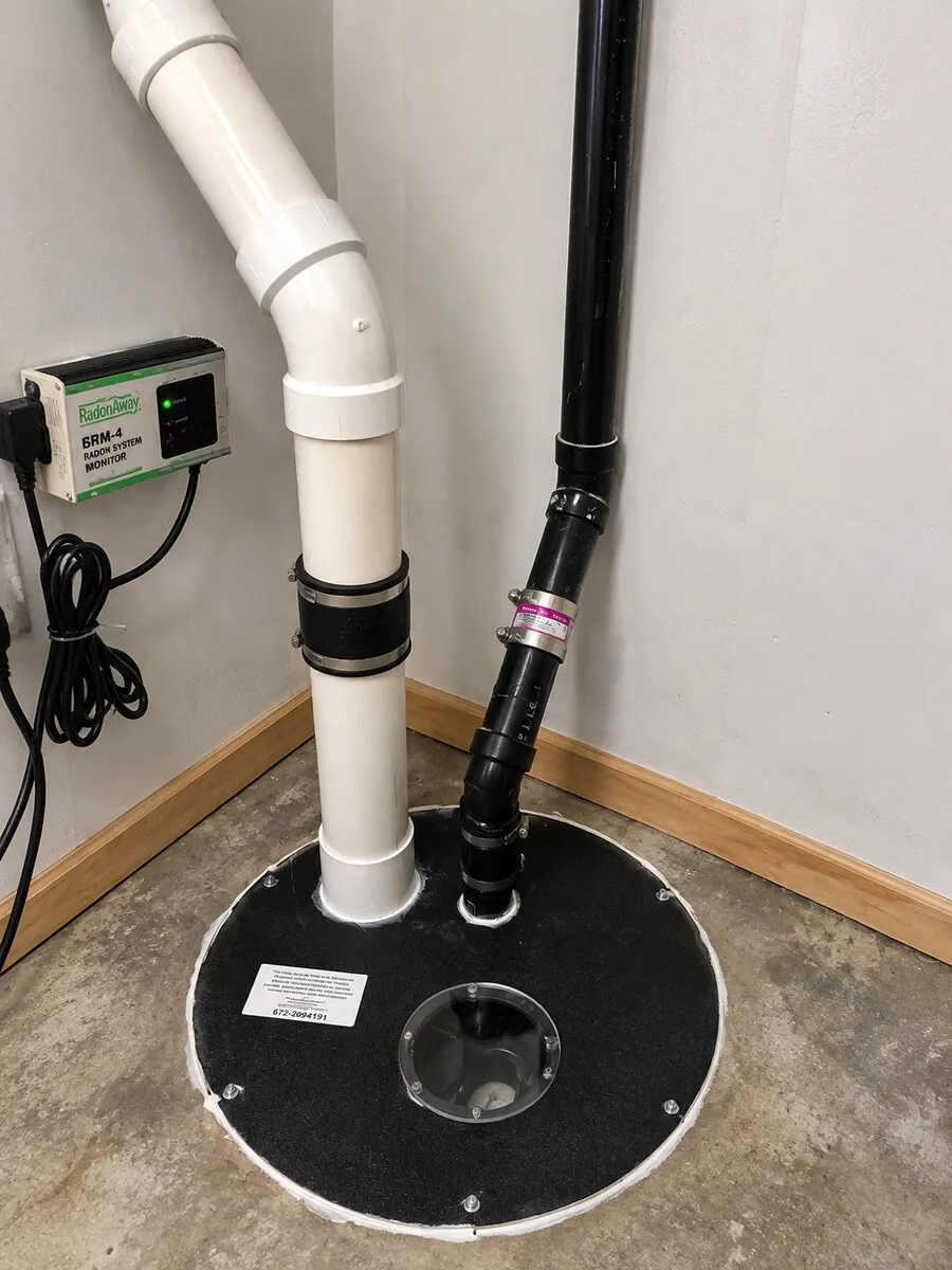 Interior radon mitigation pipes and system monitor beside a sealed sump cover